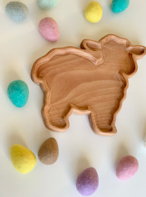 Wooden lamb-shaped sensory tray surrounded by pastel-colored felt eggs on white surface
