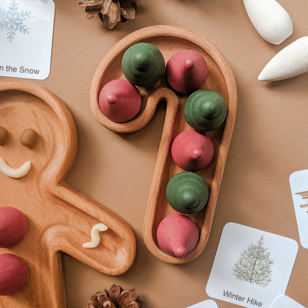 Small wooden candy cane shaped sensory tray with red and green painted wooden pegs on tan surface