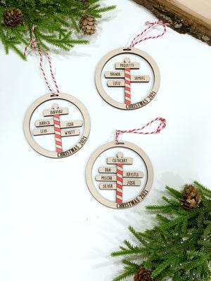 Round wooden North Pole Christmas ornaments with red striped pole and personalized family names on white background
