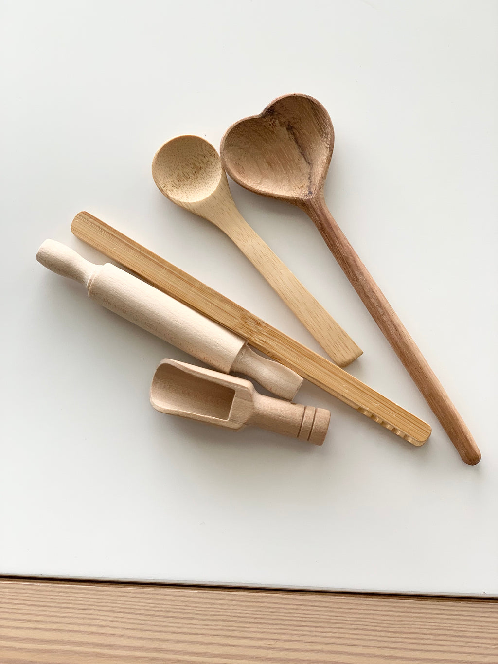Set of natural wooden sensory bin tools including heart-shaped spoon, round spoon, scoop, rolling pin, and stick on white background